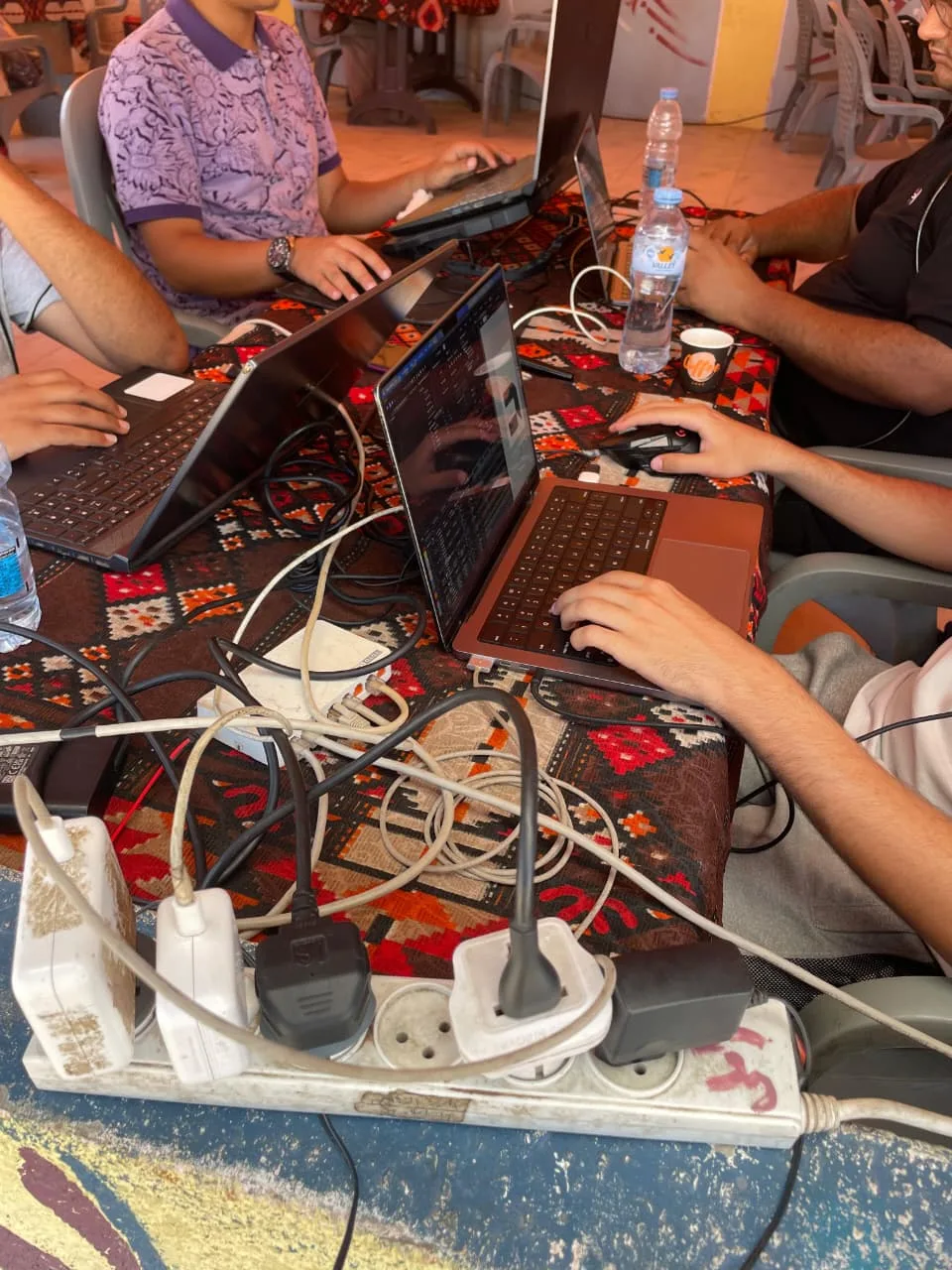 Several laptops on a shared table, all drawing power from a single multi-outlet strip in the foreground