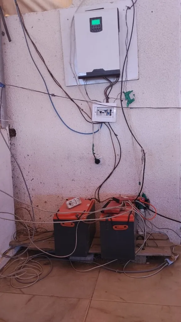 A wall-mounted solar inverter above two batteries connected by a dense bundle of cables