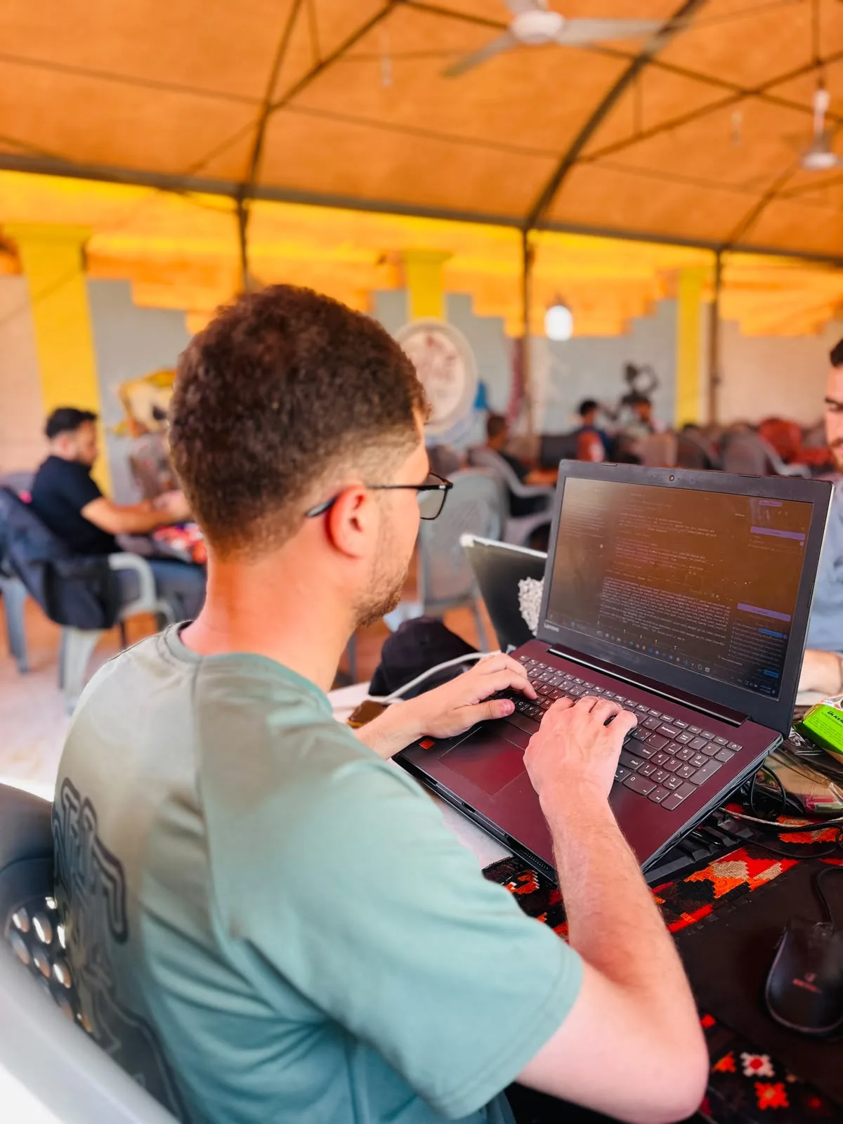A student at a laptop with rows of others working behind, under the tented roof of the Riva Hub hall